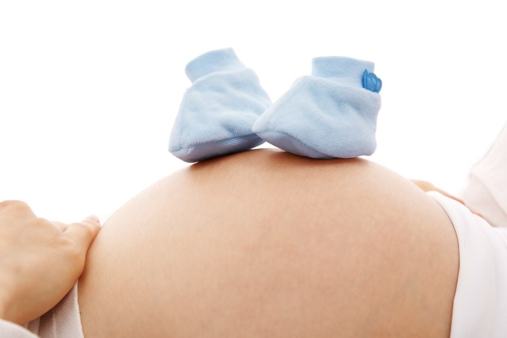 A baby bump with a pair of baby booties resting on top.