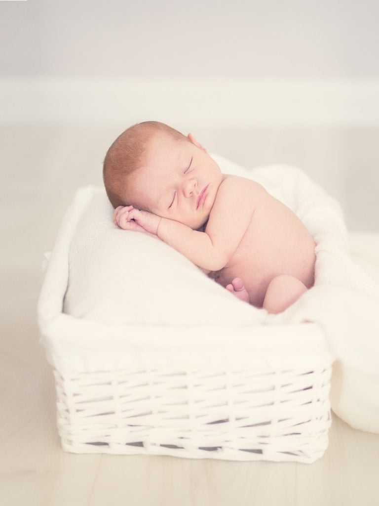 A newborn baby taking a nap in a pillowed basket.