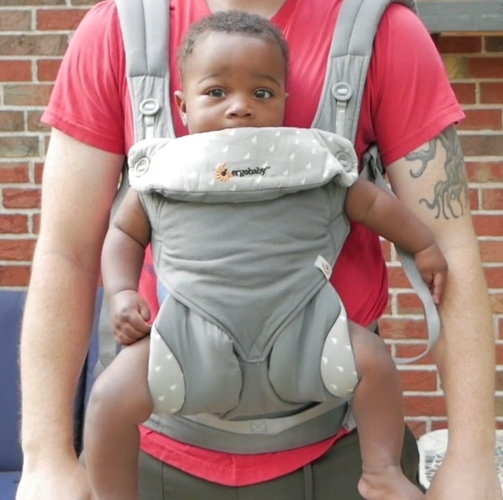 A baby in the Ergobaby 360 carrier being carried by a guy with a red shirt