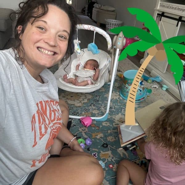 The author sits on the floor with her newborn and toddler. A palm tree is superimposed onto the picture