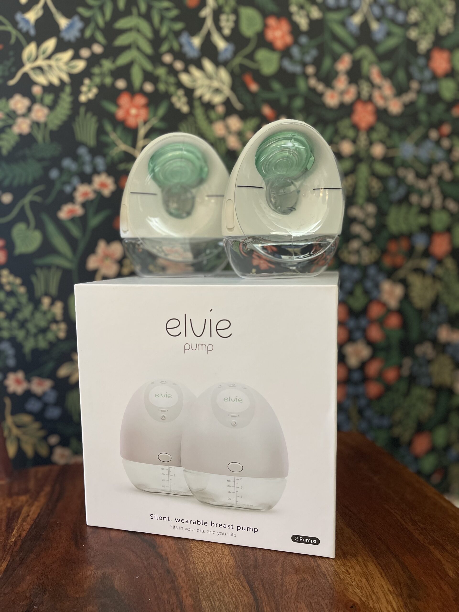 Elvie wearable breast pump sits on top of an Elvie box against a flowery wallpaper background