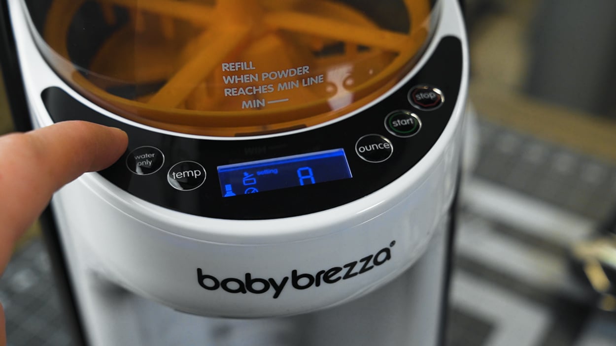 A finger touching the controls of the Baby Brezza Formula Pro Advanced