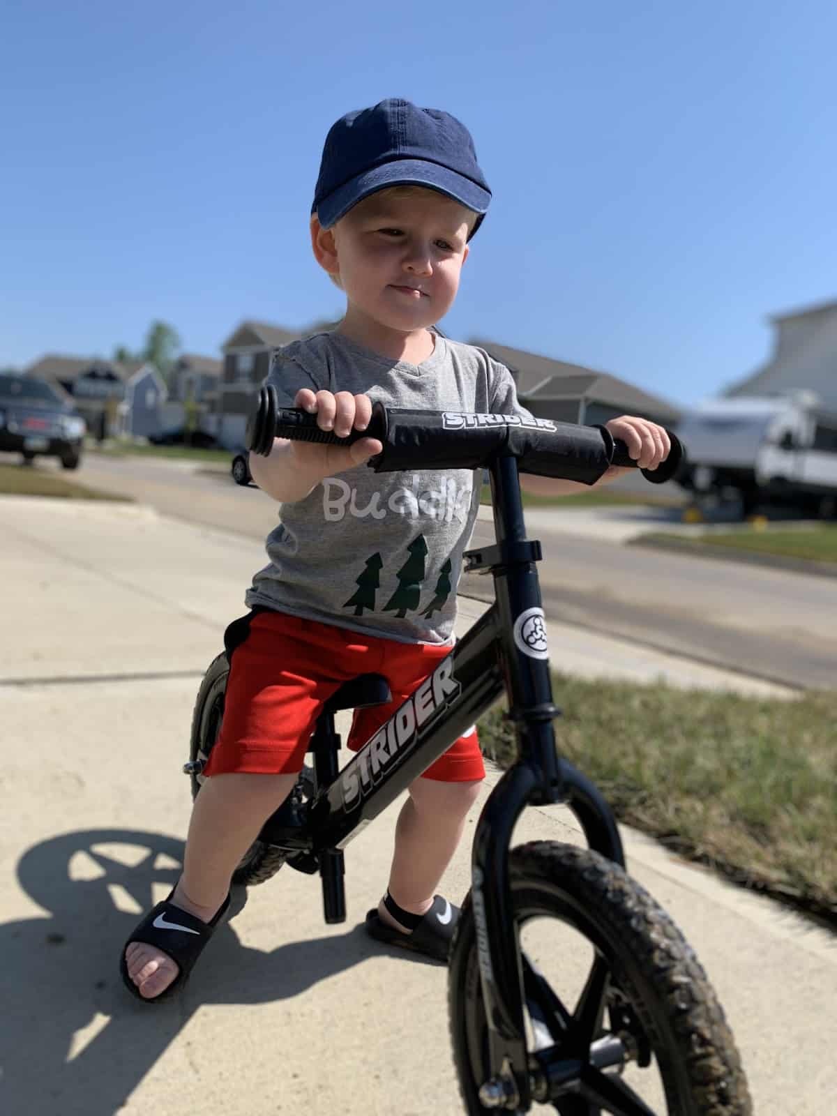 A kid on a Strider Bike on a suburban sidewalk