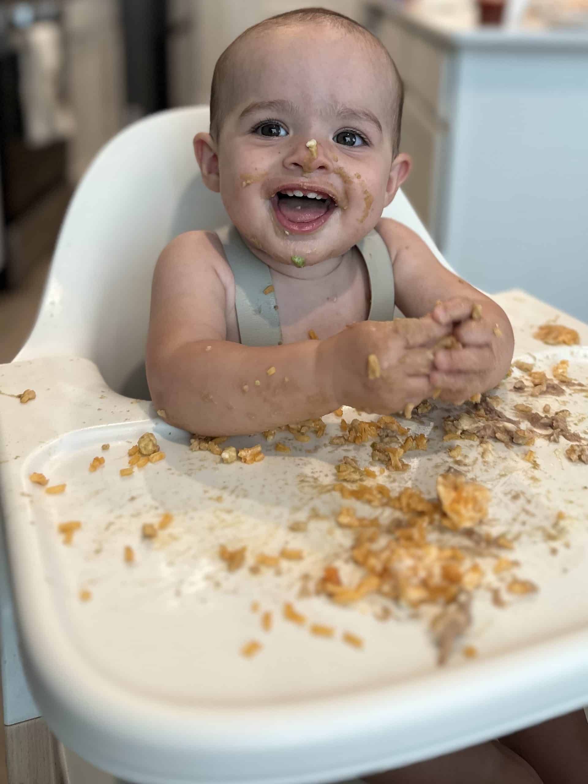 a baby sits in the Mockingbird high chair, smiling