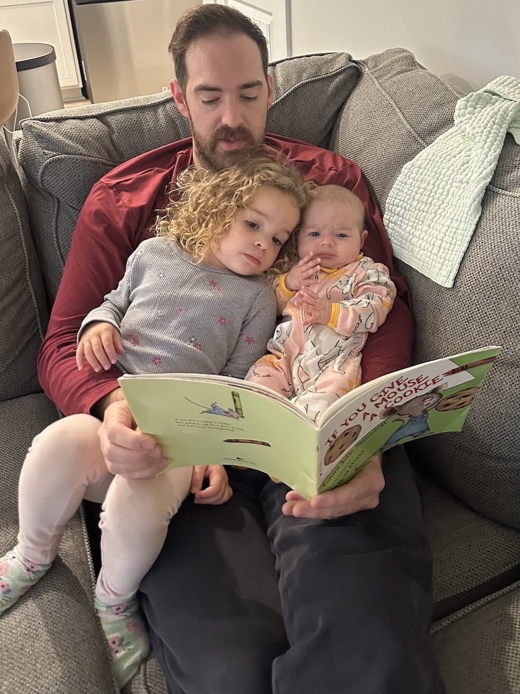 A dad reads to a newborn and a toddler