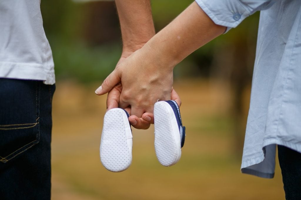 A couple holding hands with baby booties hanging down.