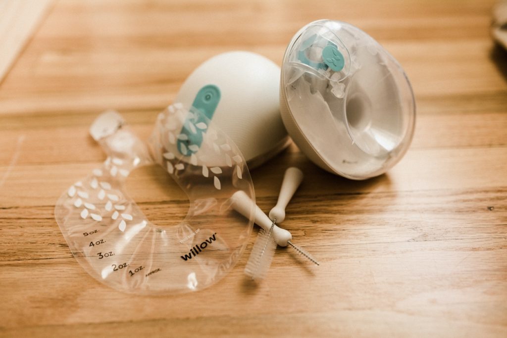 A Willow breast pump on a table with milk bag and cleaning brushes