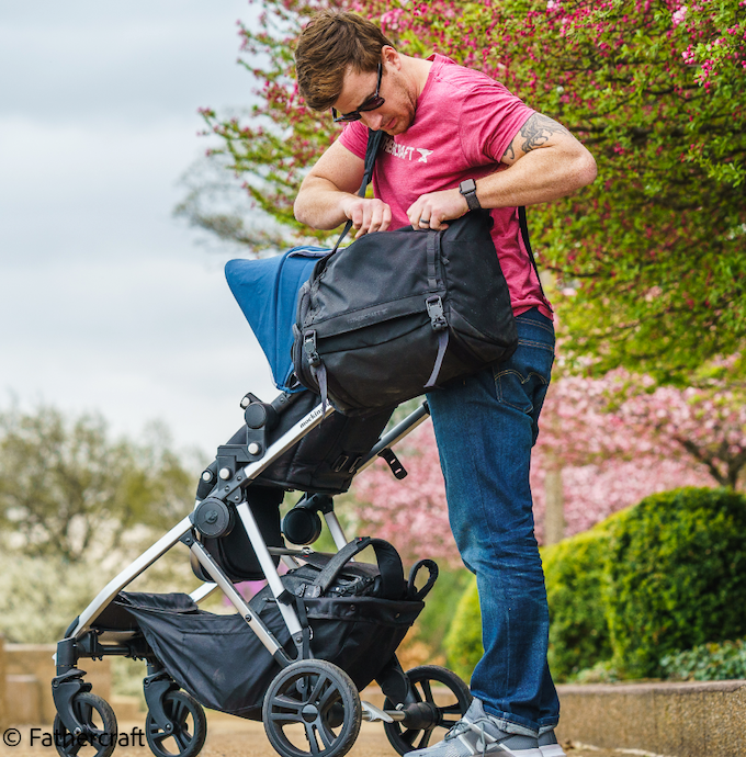 A dad digs around in a diaper bag while standing next to a stroller