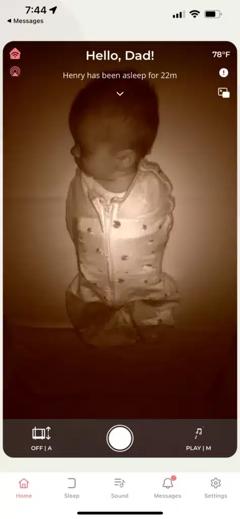 A screenshot of the Cradlewise app showing baby Henry asleep in the bassinet. The text on the screenshot says, "Hello, Dad! Henry has been asleep for 22m" 