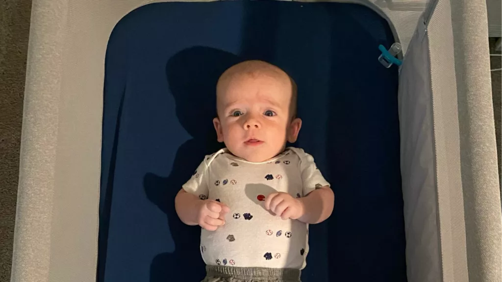 Newborn baby lies awake on his back in a Newton Bassinet with blue sheets